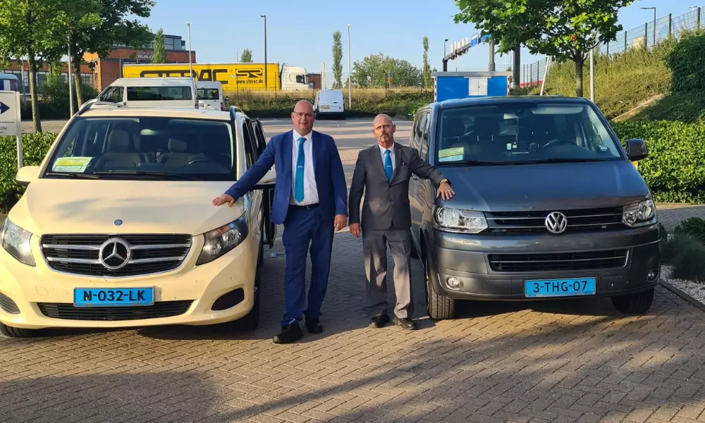"Twee taxichauffeurs in pak bij hun voertuigen van Regio Taxi Spijkenisse"